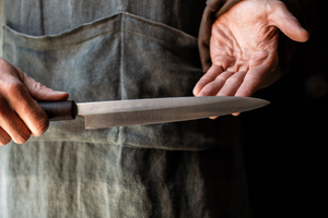 A person holding a traditional Japanese kitchen knife with a long, slender blade and a dark wooden handle.